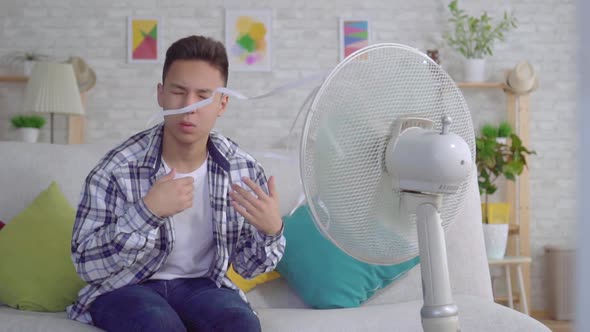 Young Asian Man Sitting in Front of a Working Fan the Concept of Heat Slow Mo