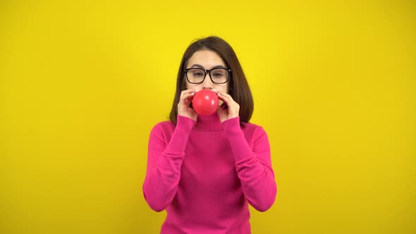 A Young Woman Inflates a Red Balloon with Her Mouth on a Yellow Background. Girl in a Pink