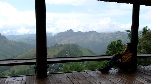 A female traveler sitting and looking at a beautiful mountains and nature view on wooden balcony.