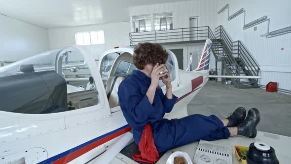 Female Aircraft Mechanic Drinking Tea while Having Lunch in Hangar