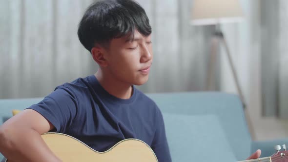 Close Up Of Asian Boy Composer With Notebook On Table Playing Guitar At Home