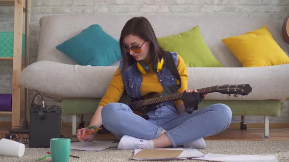 Young Woman Rocker Musician Writes Music on Electric Guitar Sitting on the Floor