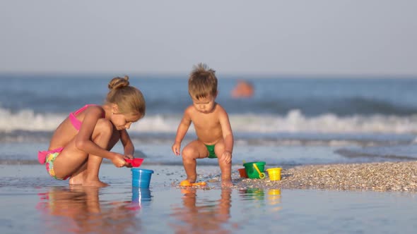 Older Sister Playing with Younger Brother Aground Near the Shore on Summer Vacation