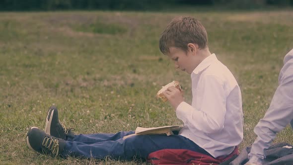 Boy in White Shirt Sits on Grass and Eats Tasteless Sandwich