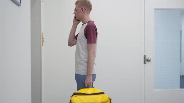 Side View Portrait of Young Caucasian Man Talking on Phone Waiting for Lift with Yellow Food