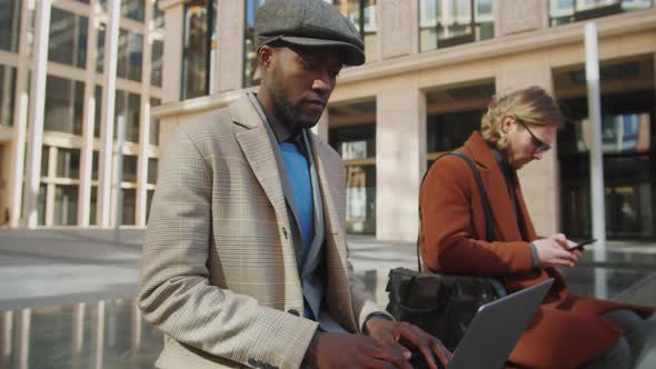 Two Multiethnic Businessmen Using Laptop and Smartphone Outdoors