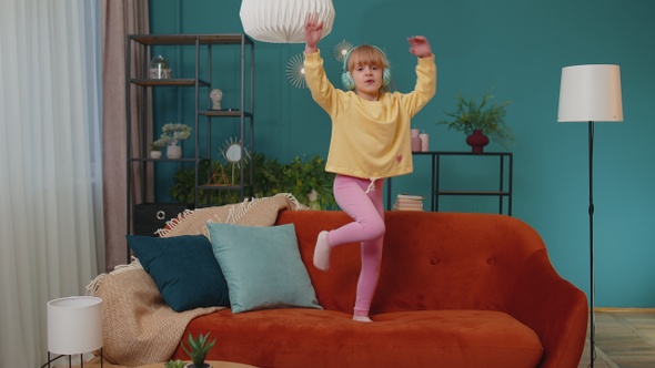 Happy Child Girl Kid in Headphones Dancing and Jumping While Listening to the Music at Home Alone