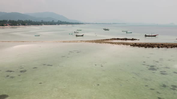 Drone flying over empty wooden boats standing on turquoise sea at low tide on asian paradise beach