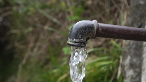 Clean water pours from an old rusty pipe in nature