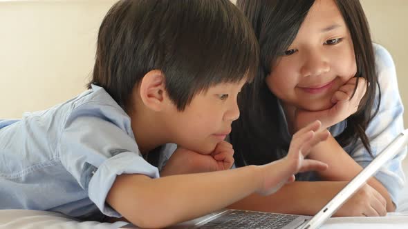 Cute Asian Children  Lying In Bed And Using Laptop On White Bed