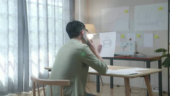 Back View Of A Man Designer Talking On Smartphone While Looking At Sketching Layout Bond In Hand