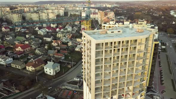 Aerial view of concrete frame of tall unfinished apartment building under construction in a city.