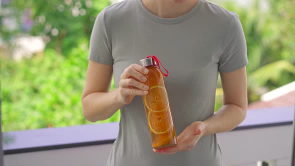 A Woman Holds a Bottle of Kombucha Drink in Her Hands Which Has an Orange Flavor