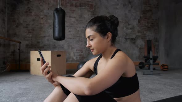 Young Indian Girl Looking smart phone for the Exercise Workout in the gym. A woman Rests during