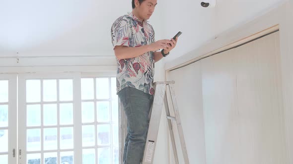 Asian Man On A Ladder Use Mobile Phone Control Security Cctv Camera