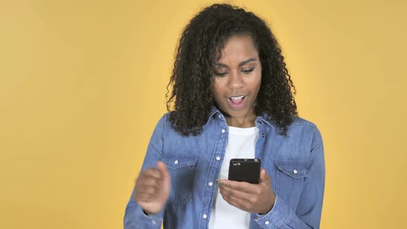 African Girl Excited for Success While Using Smartphone Isolated on Yellow Background