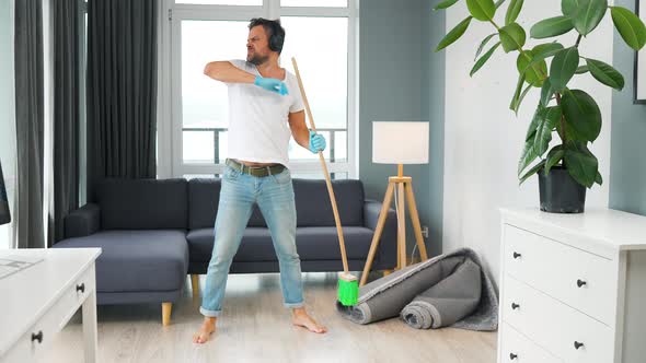 Man in Headphones Cleaning the House and Having Fun Dancing and Singing with a Broom