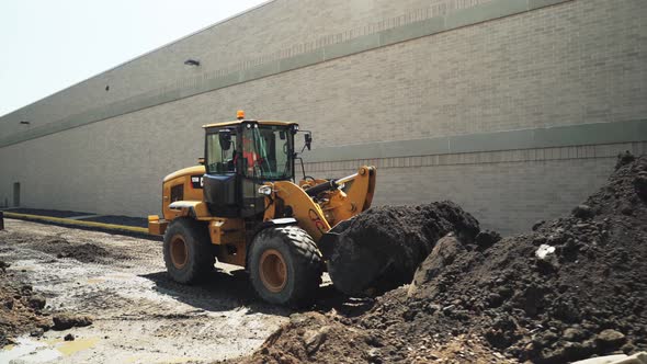 Front loader construction truck scooping dirt soil on foundation construction site