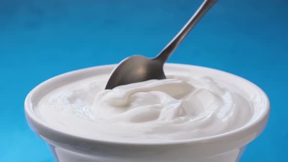 Bowl of sour cream on blue background, greek yogurt