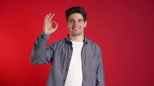 Handsome Young Man in Denim Shirt Smiles To Camera. Hipster Guy Showing OK 