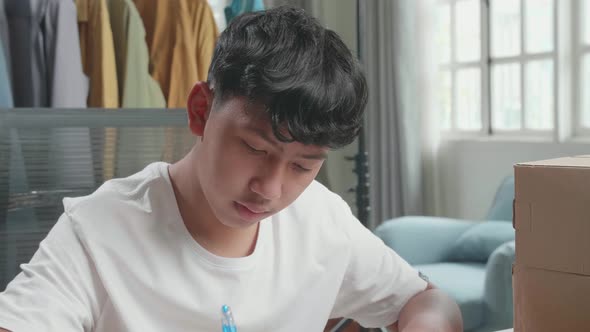 Close Up Of Asian Man Online Seller With Package Writing In The Notebook While Selling Clothes