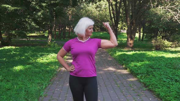 Mature woman in sportswear shows her biceps and muscles, showing her strength and self-confidence.
