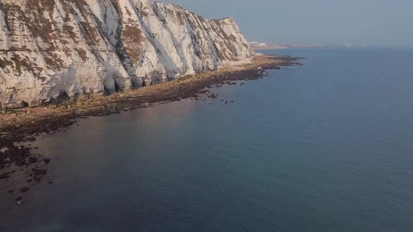 Drone flies low towards the White Cliffs of Dover with camera panning up. Beautiful turquoise sea in