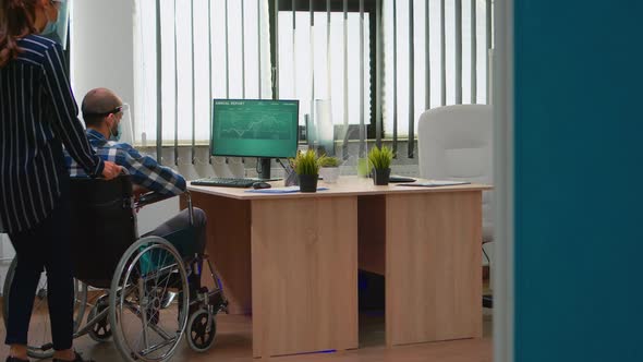 Woman with Protection Mask Helping Disabled Man to Get at Desk