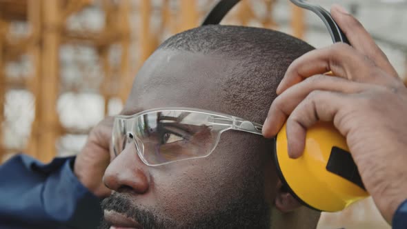 Black Male Worker Putting On Noise-Canceling Earmuffs