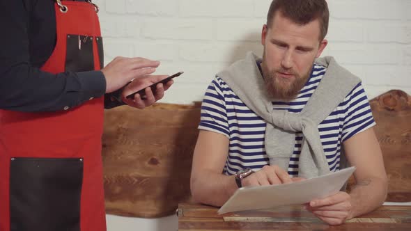 Bearded Man Is Ordering Meal in Cafe, Showing To Waiter on Menu