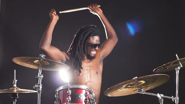 Good-looking Artistic African Drummer with Dreadlocks Sit Beating on Drums with Sticks