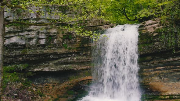 Scenic Drone Shot of a Small Fresh and Fast Cascade in the Forest Spring Green Vegetation Aerial