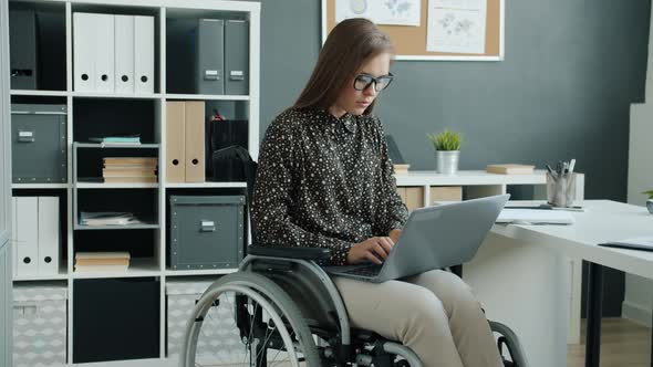 Paraplegic Office Worker in Wheelchair Using Laptop Typing Working Concentrated on Business Activity