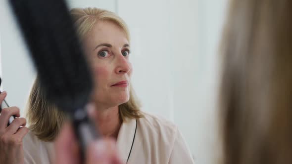 Caucasian senior woman looking in bathroom mirror combing her hair