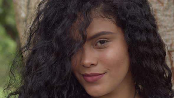 Close up of a young woman with red lipstick smiling with a large tree trunk in the background