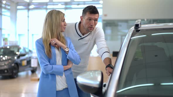 Positive Beautiful Woman and Handsome Man Talking Choosing New Automobile in Car Dealership