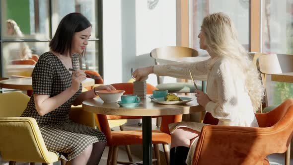 Side View of Relaxed Slim Caucasian Women Talking and Eating in Cafe on Lunch Break