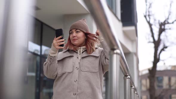 Lowangle View of Beautiful Happy Young Plus Size Woman Wearing Warm Outerwear and Hat Taking Selfie