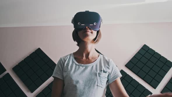 Young Woman in a Virtual Reality Headset Plays a Game at Home