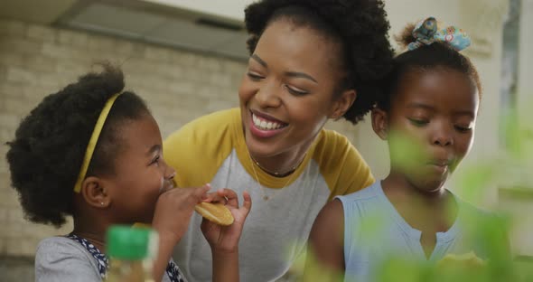 Happy african american mother with daughters eating in kitchen