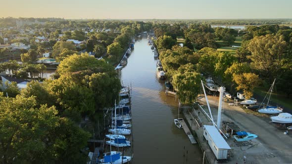 Aerial following a river path with several boats docked and at sides some houses. Dolly in