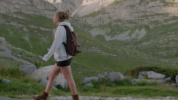 Happy millennial woman with dreadlocks and backpack walking through mountain valley