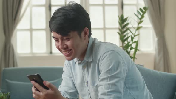 Male Using Smartphone And Smiling In Living Room