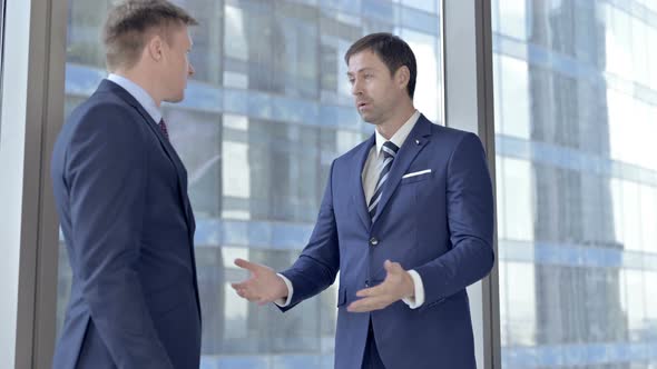 Upset Two Middle Aged Businessmen Having Arguments Against Boardroom Office Window
