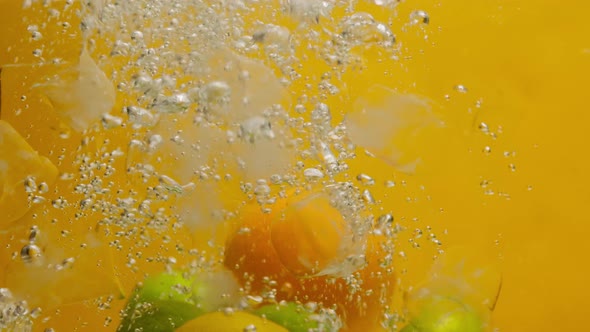 Closeup of Falling Limes Oranges and Lemons Into the Water with Ice on Orange Background Making a