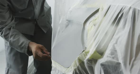 African American male car mechanic taking a protective cover off a car