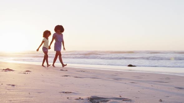 African american mother and daughter having fun walking together on the beach