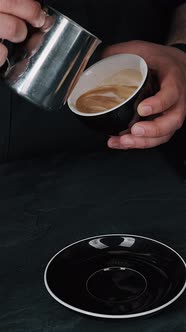 Barista pouring milk in hot coffee and making cappuccino foam in cafe close up, vertical