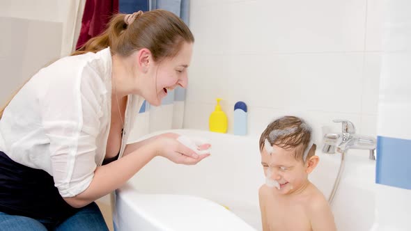 Happy Smiling Mother and Little Boy Playing with Soap Foam in Bath at Home