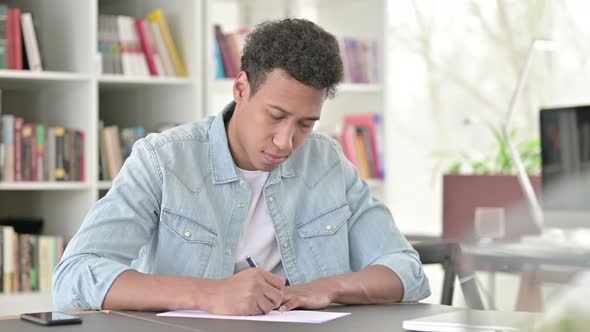 Young African American Man Writing on Paper at Work 